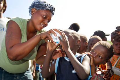 Sharlene Jean offers a sample of treated drinking water to a child living in a makeshift camp in Gresier, Haiti. The United Methodist Committee on Relief and partner agencies provided water treatment supplies to the camp. Photo by Mike DuBose, UMNS.