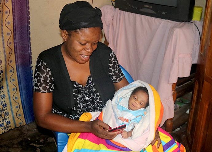 Safi Zamuda holds her baby while looking at a text from the United Methodist Health Center in Irambo, Democratic Republic of Congo. As part of the UMConnect program, the hospital sends alerts to new and expectant mothers to remind them of upcoming appointments. Zamuda said she is thankful for the messages and her healthy child. Photo by Philippe Kituka Lolonga, UMNS.